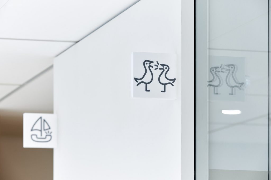 Foto der Signaletik im neuen Bürogebäude der Haspa: im Vordergrund ein Piktogramm von zwei Möwen, die sich "unterhalten"; ein weiteres zeigt ein Boot in Form eines Telefons mit Segeln.